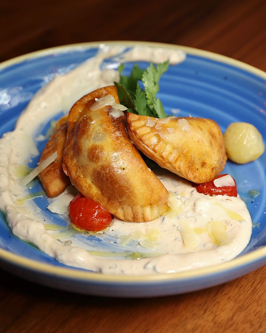 Three small, golden-brown empanadas are served on a thick swoosh of creamy sauce on a blue plate.