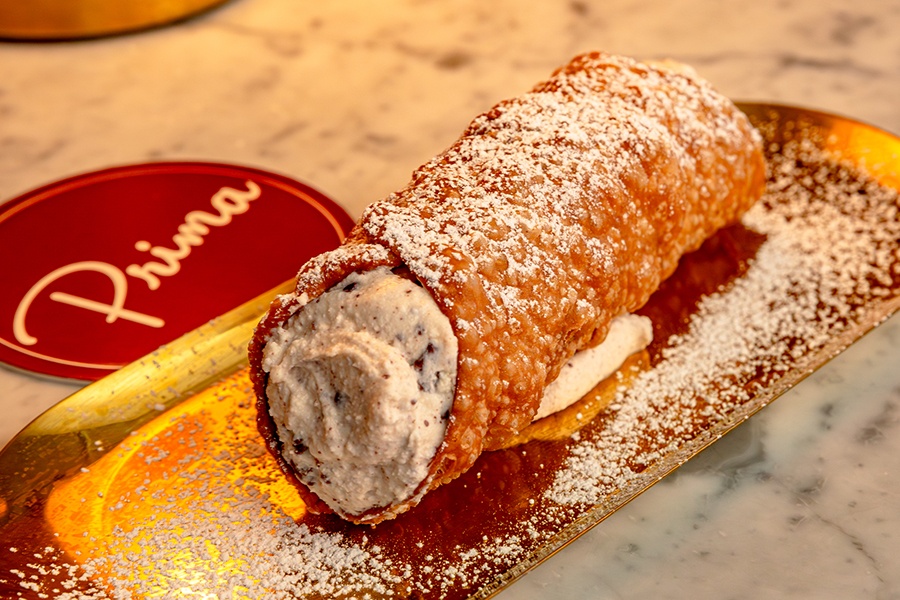 A large cannoli topped with powdered sugar sits on a golden tray.