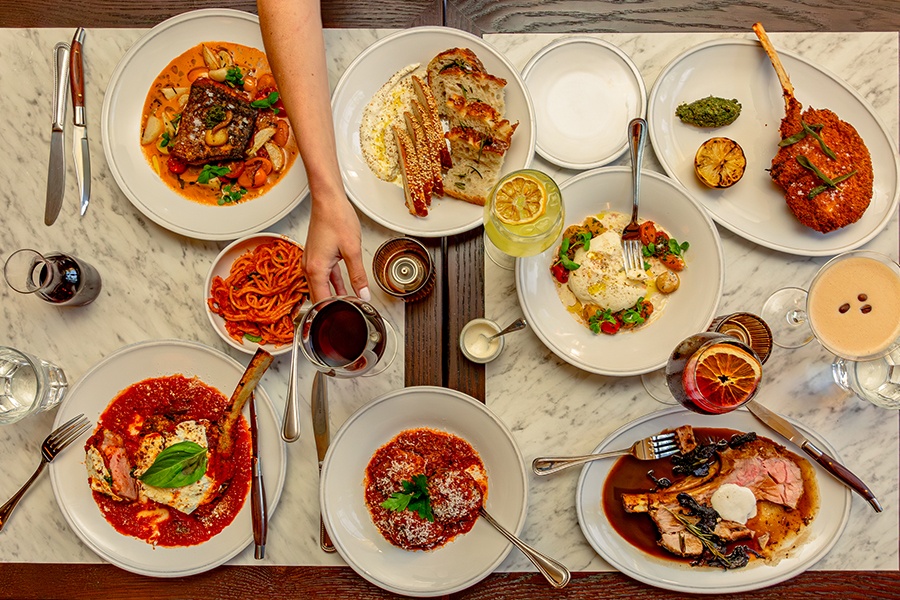 Overhead view of a white marble table covered with pasta, steak, and other Italian dishes.