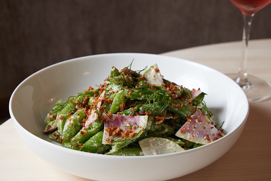 Snap peas topped with fresh dill, breadcrumbs, and thin radish slices are served in a white bowl.