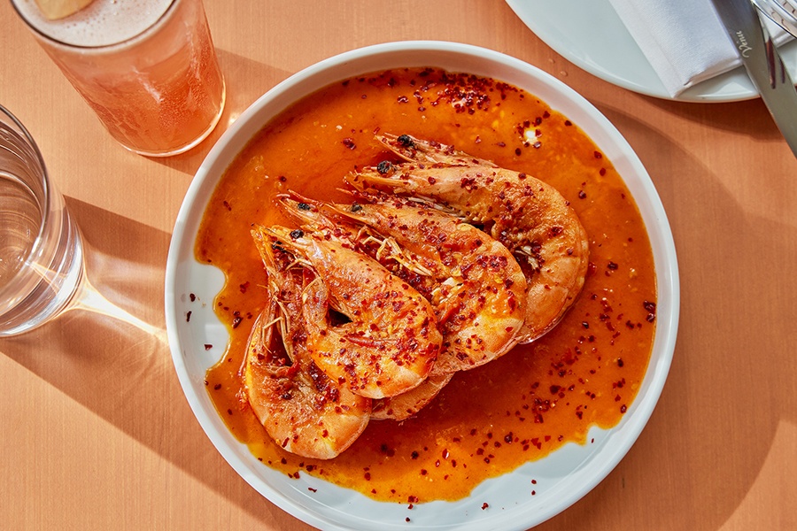 Overhead view of a plate of large shrimp, heads and tails on, in a pool of red butter.