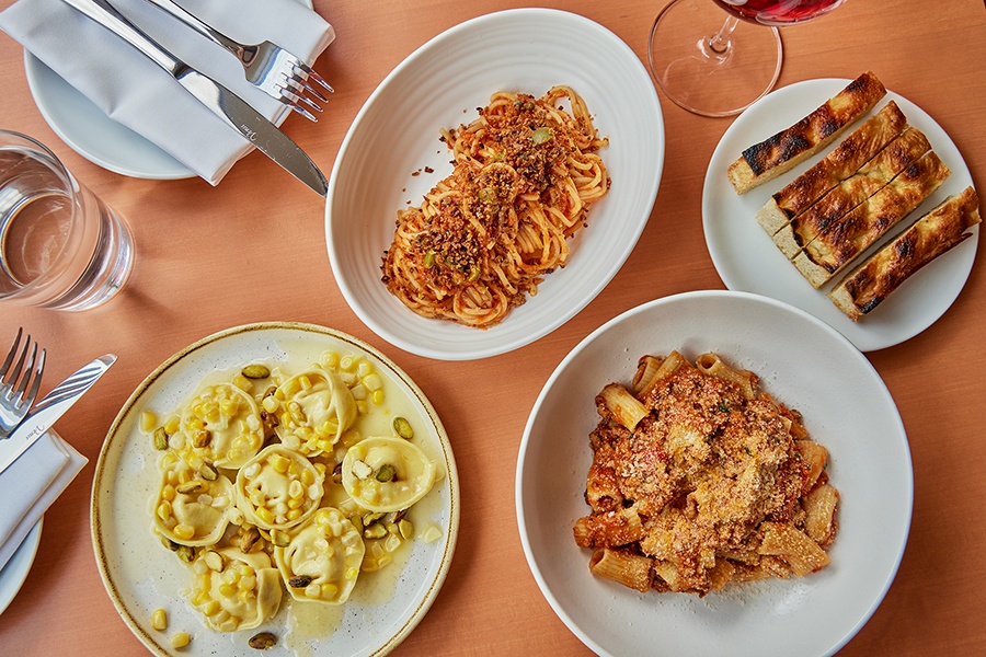 Overhead view of three different pastas on white plates and a side of focaccia-like fried dough.