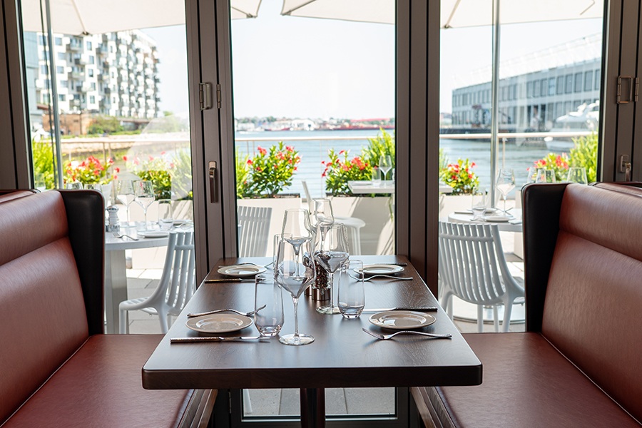 A brown leather booth at a restaurant is next to large windows looking out onto a waterfront patio.