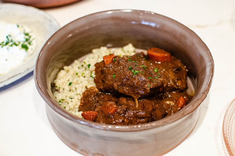 Braised beef in a brown sauce is plated in a brown bowl with a rice-like grain.