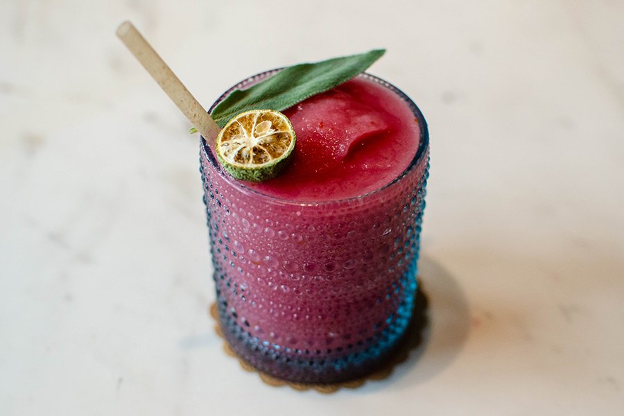 A pink frozen cocktail is topped with a sage leaf and dried kumquat.