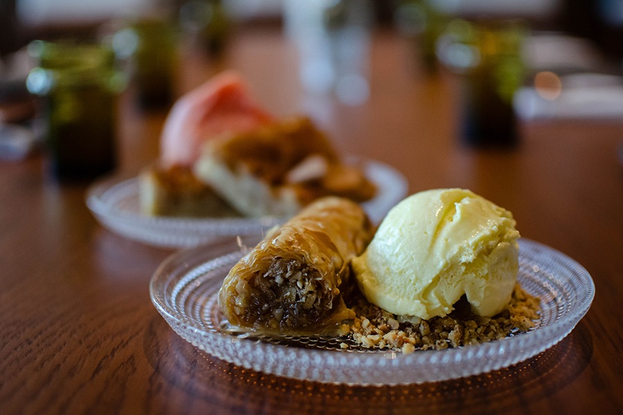 A rolled-up version of baklava with a big scoop of ice cream sits on an elegant glass plate.