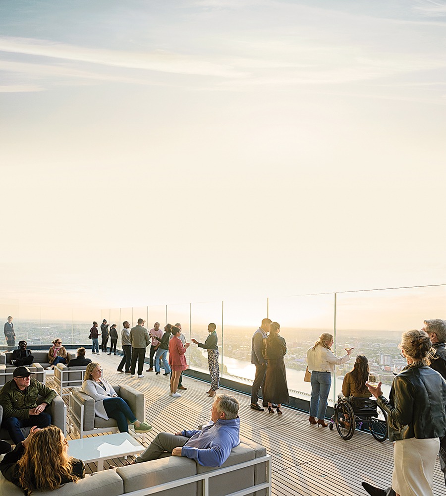 People sit on a roofdeck and look out into sunny skyline views from behind large glass barriers.