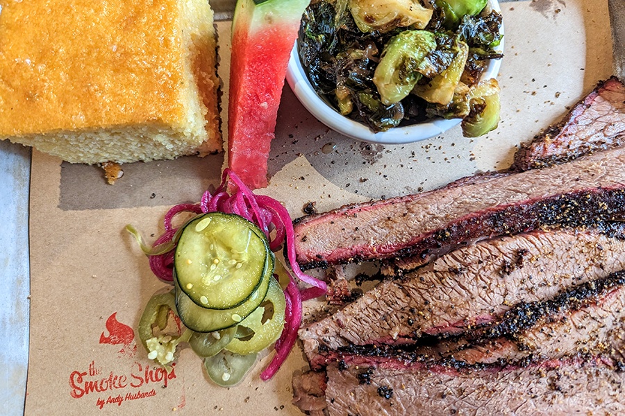 Overhead view of brisket, cornbread, watermelon, and Brussels sprouts on brown paper on a silver tray.