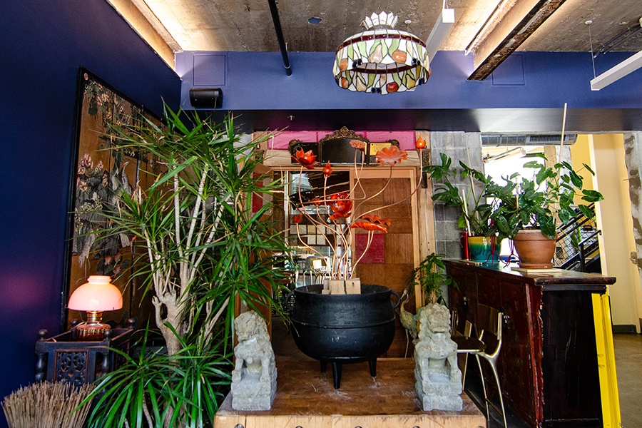 The entryway into a restaurant is decorated with plants, a vintage light fixture, stone sculptures, and more.