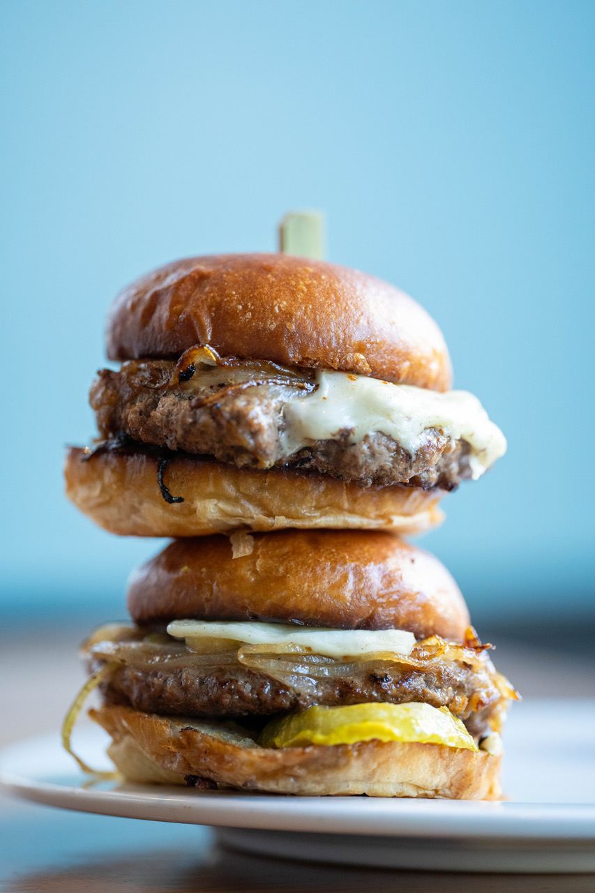 Two cheese and onion burgers are stacked on top of each other.