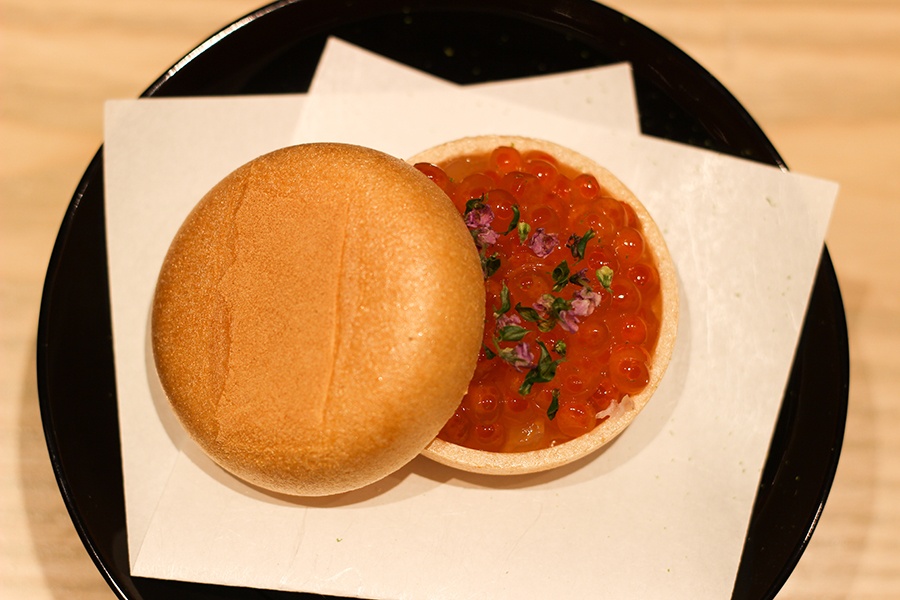 Overhead view of a round, hollowed out cracker split in two and full of salmon roe with an herbal garnish.