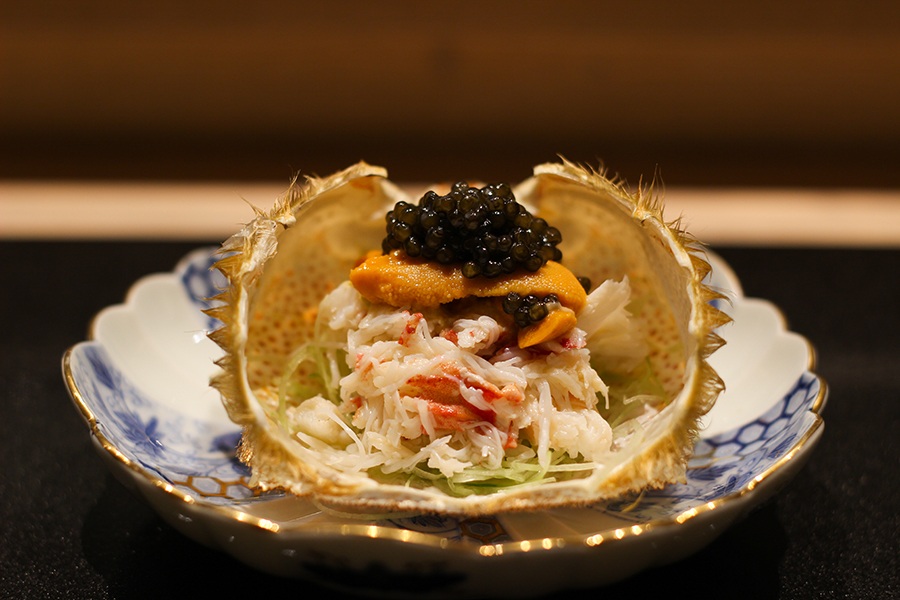 A crab shell is open to reveal crab meat topped with orange uni and a dollop of caviar.