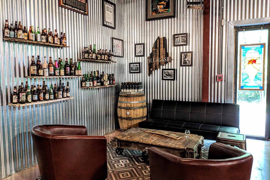 A brewery taproom has aluminum walls, beer bottles on shelves, and cozy dark leather lounge seating.