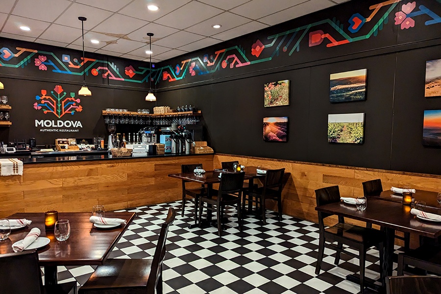 Casual restaurant interior with a black and white tiled floor. The walls are painted black with a colorful floral border.