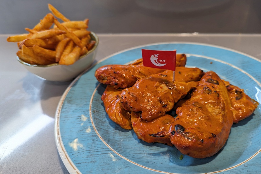 A plate of grilled chicken tenders in a thick orange sauce is garnished with a little red flag on a toothpick that says "hot" with a chili pepper.