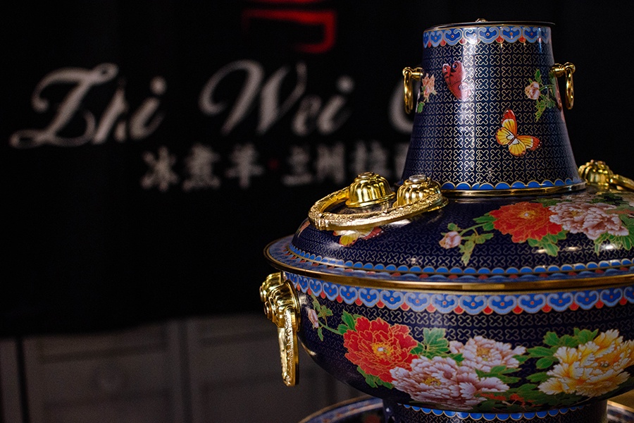 A decorative hot pot at a Chinese restaurant is covered with colorful flowers. A banner in the background says Zhi Wei.