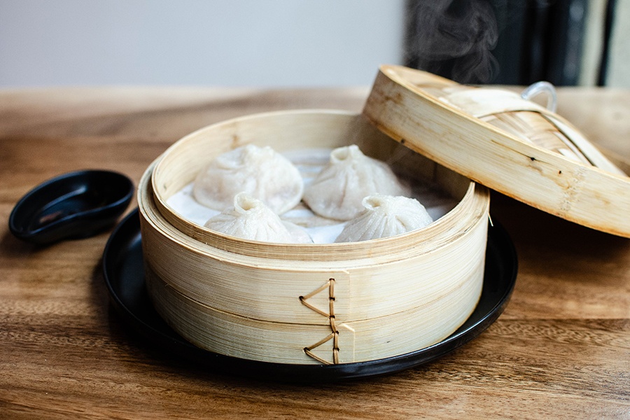 A wooden steamer basket is open to reveal four soup dumplings.