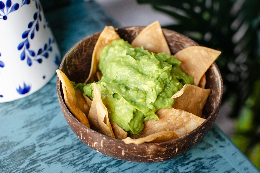 A coconut-shell bowl is full of tortilla chips topped with thick green guacamole.
