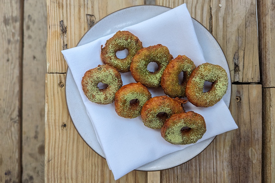 Eight little crispy doughnuts topped with a light green power sit on a white napkin on a white plate.