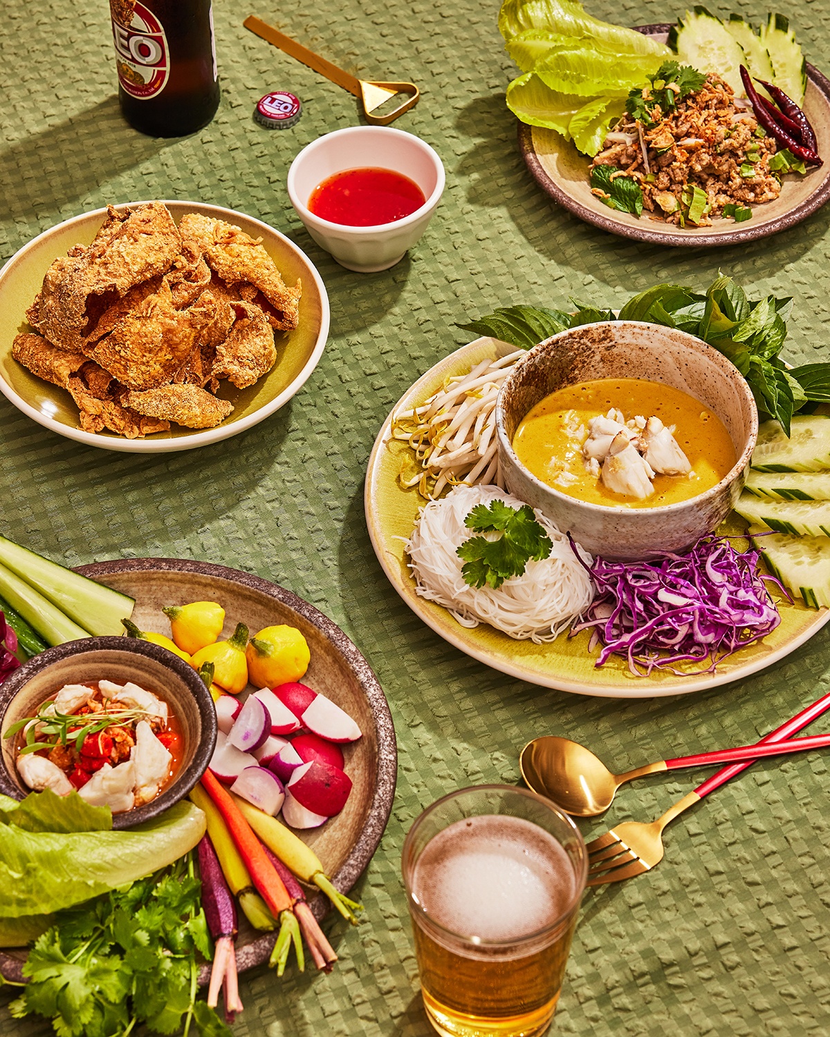 A spread of Thai dishes sit on a green tablecloth, including crab curry, crispy chicken skin, duck larb, and more.