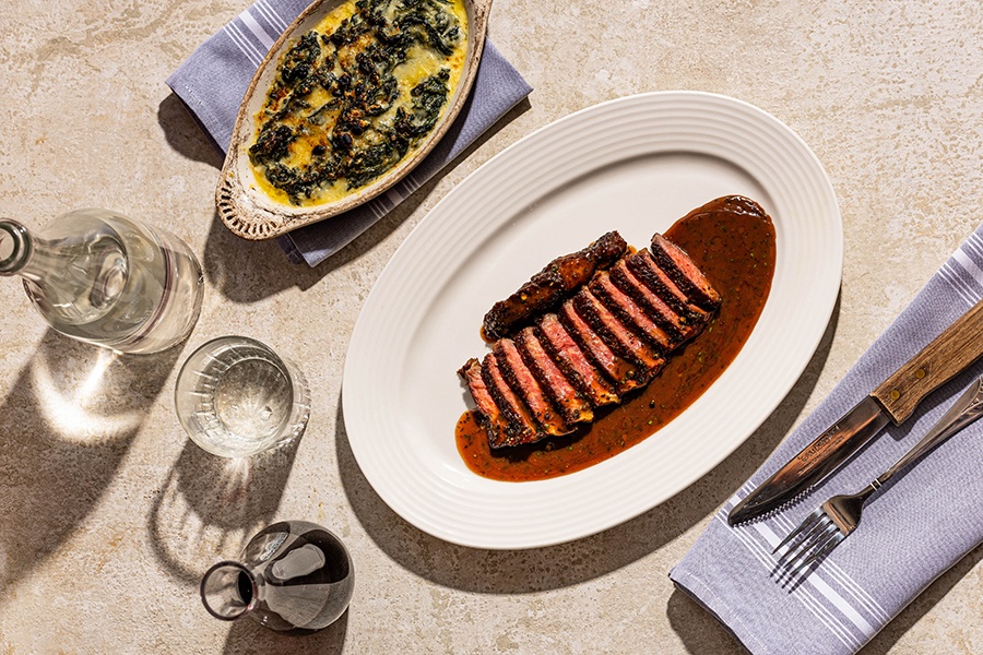 Sliced rare steak sits in a pool of brown sauce, with a side of creamy spinach.