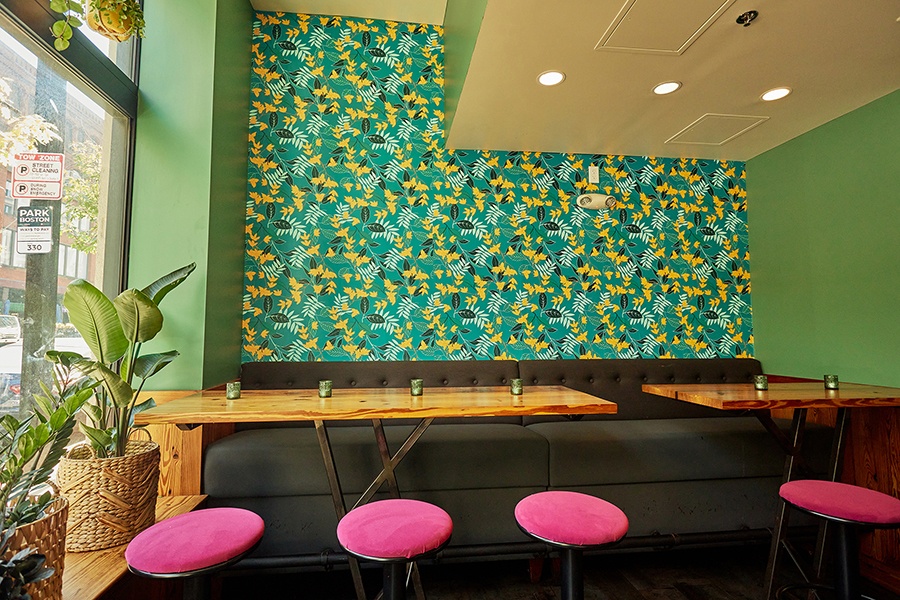 Interior of a fairly casual restaurant with tropical wallpaper, green accent walls, and pink stools.