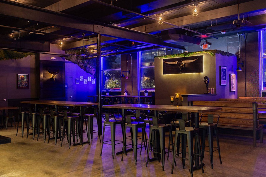 Interior of a brewery taproom with black walls and blue lighting.