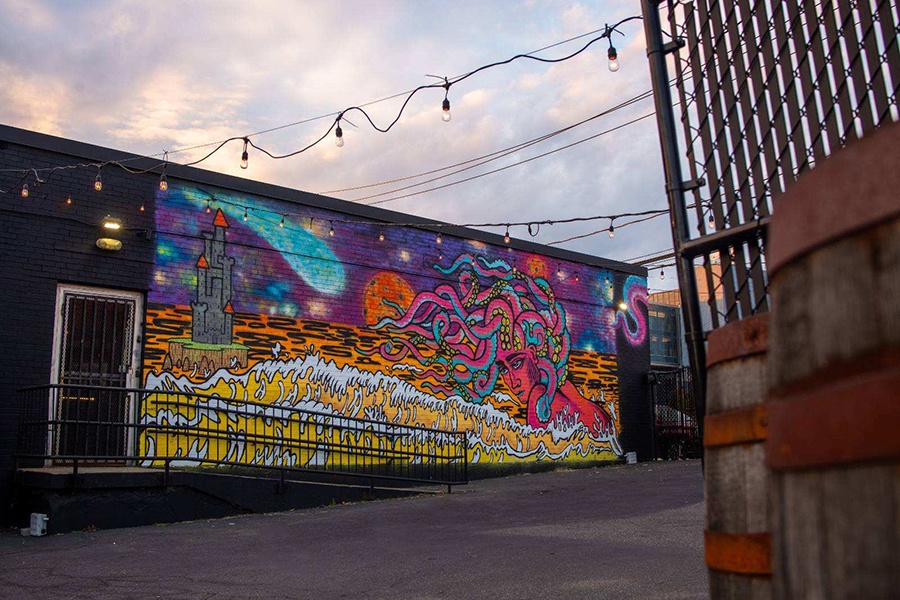 A colorful mural of Medusa and a castle is painted on the side of a one-story black brick building.