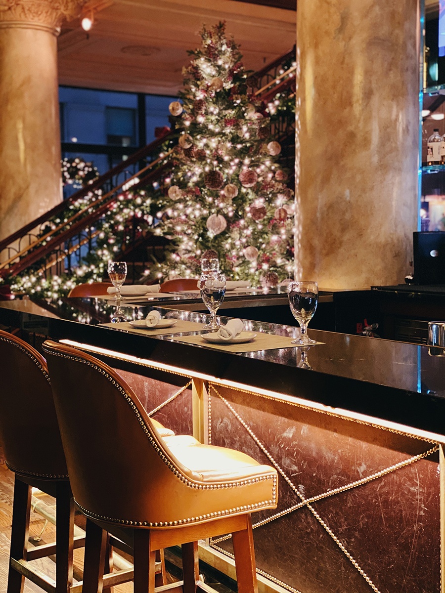 An elegant steakhouse bar area is decorated with a lit-up Christmas tree.
