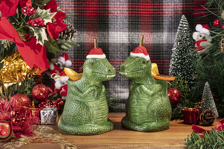 Christmas cocktails are served in T-rex-shaped glassware and surrounding by Christmas decor, like fake trees and ornaments.