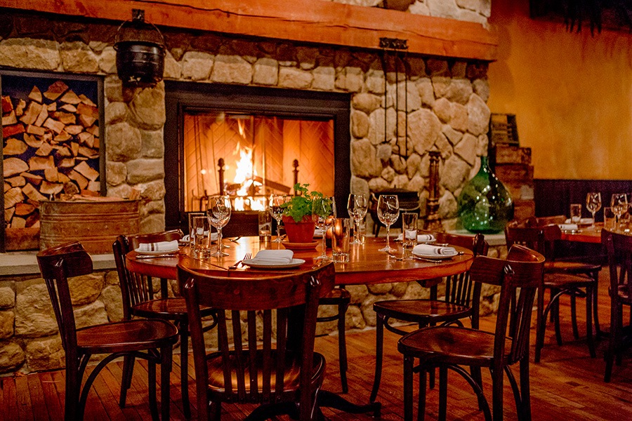 Dining table with place settings in front of lit fireplace at Capo.