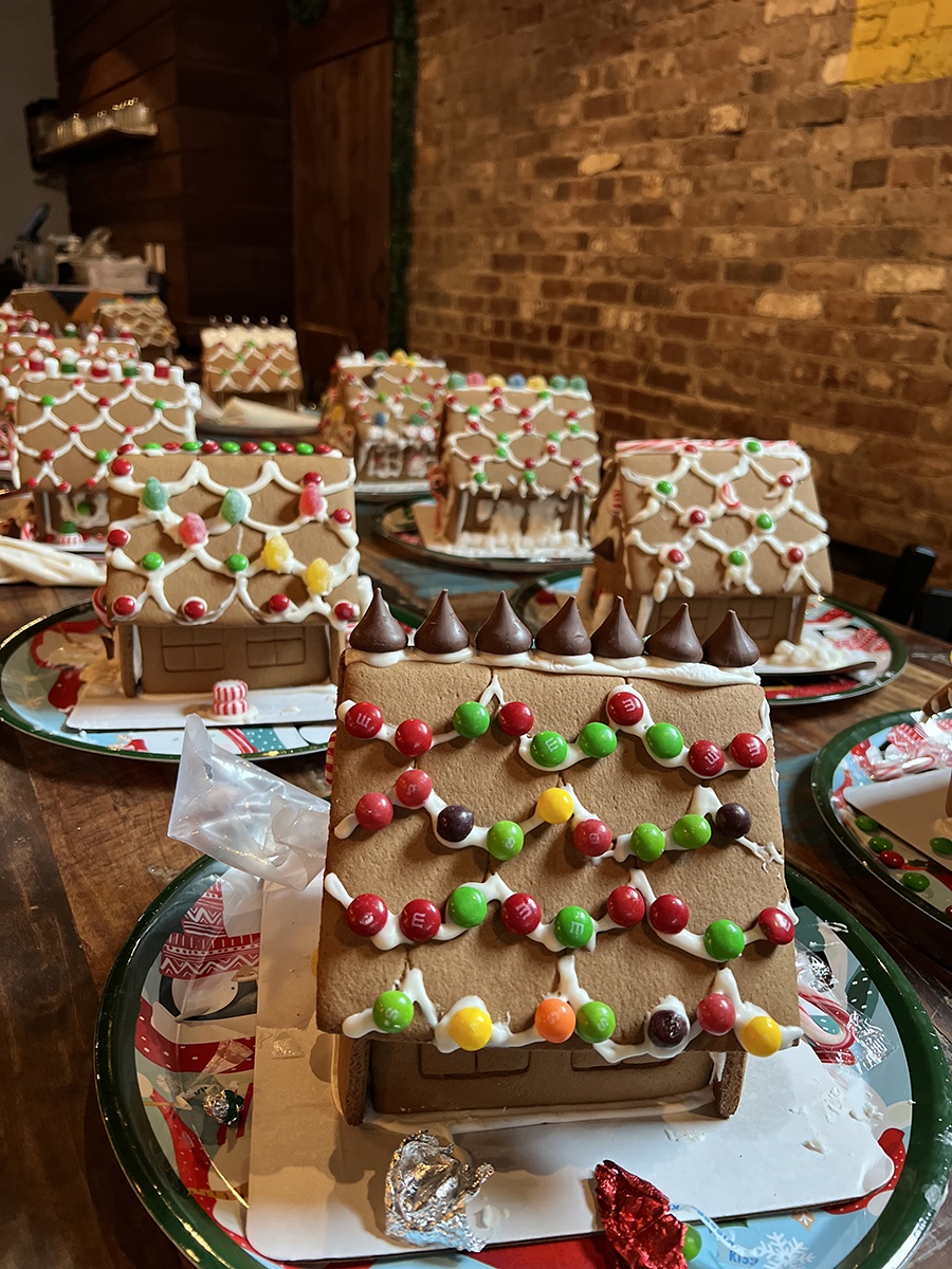 Decorated gingerbread houses are lined up in front of a brick wall.
