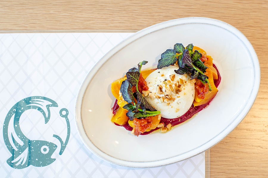Overhead view of a sphere of burrata topped with crumbled hazelnuts and accompanied by yellow beets and herbs.