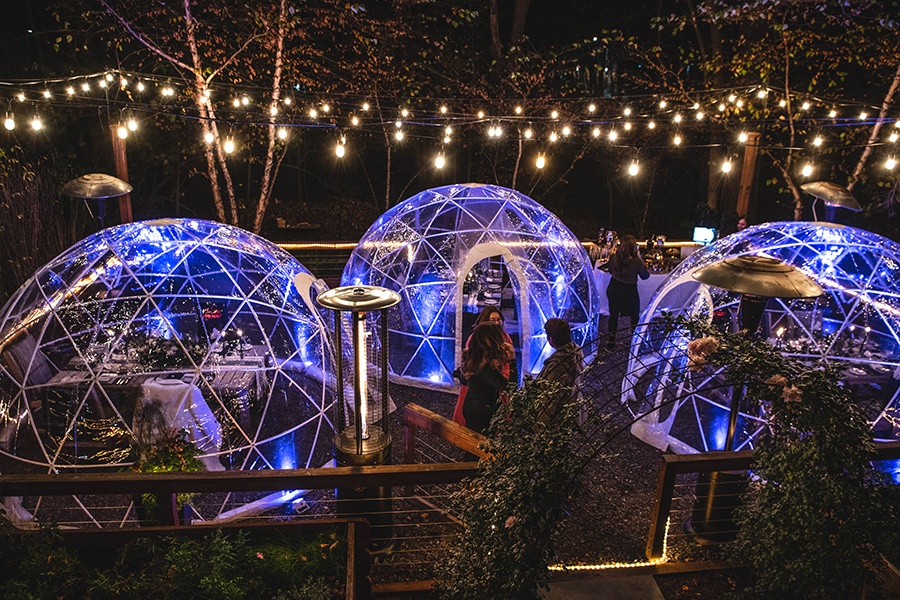 Three outdoor dining igloos are on a twinkle light-bedecked patio at night.