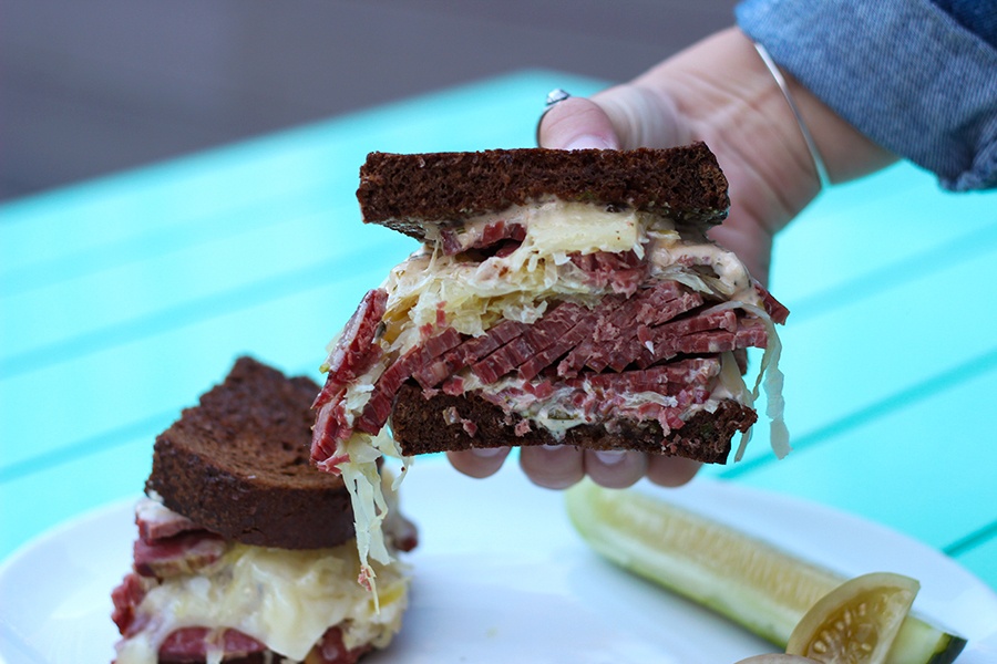 A hand holds up half of a sandwich on pumpernickel bread, with thick-sliced corned beef.