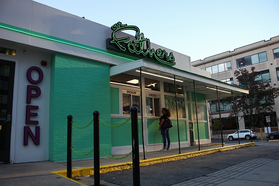 Restaurant exterior. A mint green one-story building has large lettering reading open by a door and neon, cursive signage reading Our Fathers.