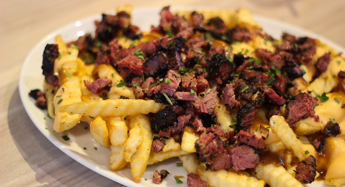 A plate of crinkle-cut fries is topped with bits of pastrami.