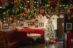 A restaurant with shiny red booths is decorated for Christmas with a tree and tons of ornament-bedecked garlands covering the ceiling.