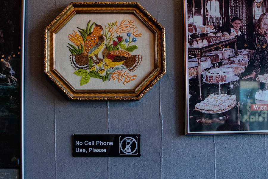 Decor at a cafe includes bird-themed embroidery and a small black sign that says "No Cell Phone Use, Please."