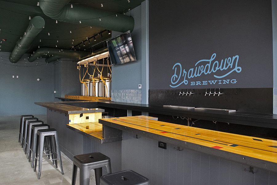 Interior of a brewery, with black stools at a light wooden bar.