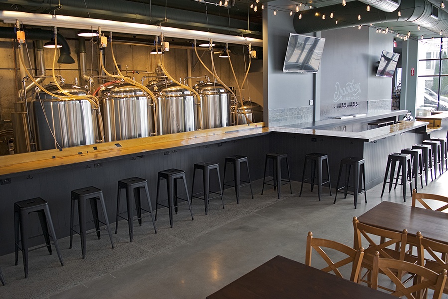 Interior of a brewery, with light wood, black stools, and string lights.