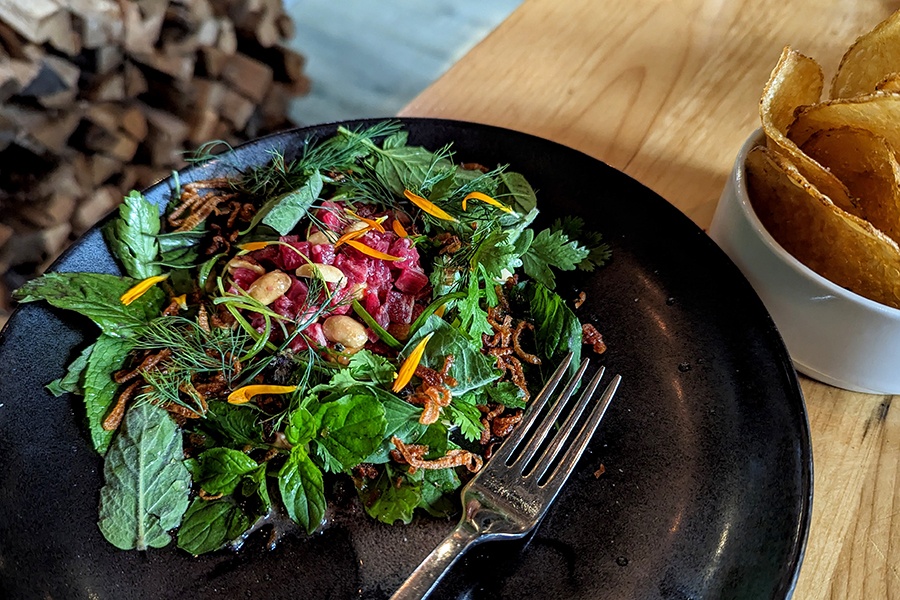 Raw beef is garnished with lots of herbs, peanuts, and fried shallots, with a side of potato chips.