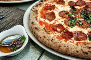 Neapolitan-style pizza topped with pepperoni and basil comes with a small side bowl of honey garnished with edible purple flowers.