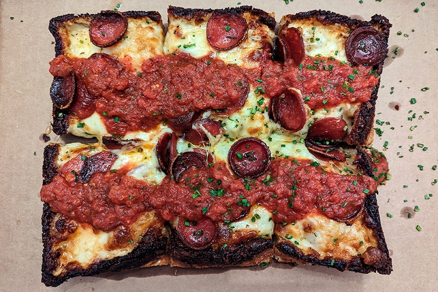 Overhead view of a rectangle of thick, cheesy pizza with pepperoni cups and thick stripes of red sauce.