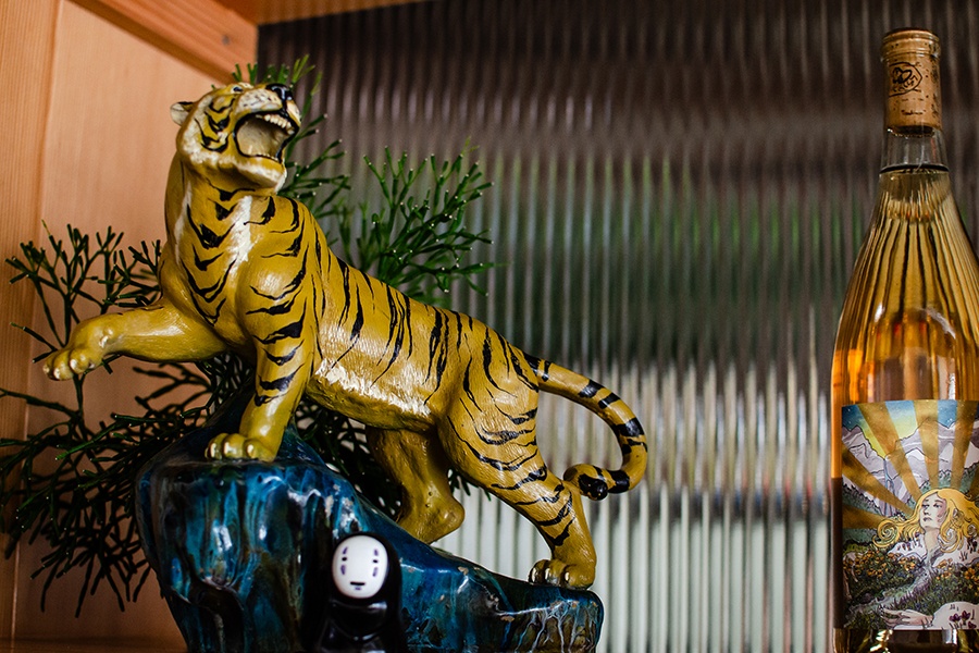 A small tiger sculpture and a Spirited Away figurine sit on a backbar next to a bottle of rose wine.