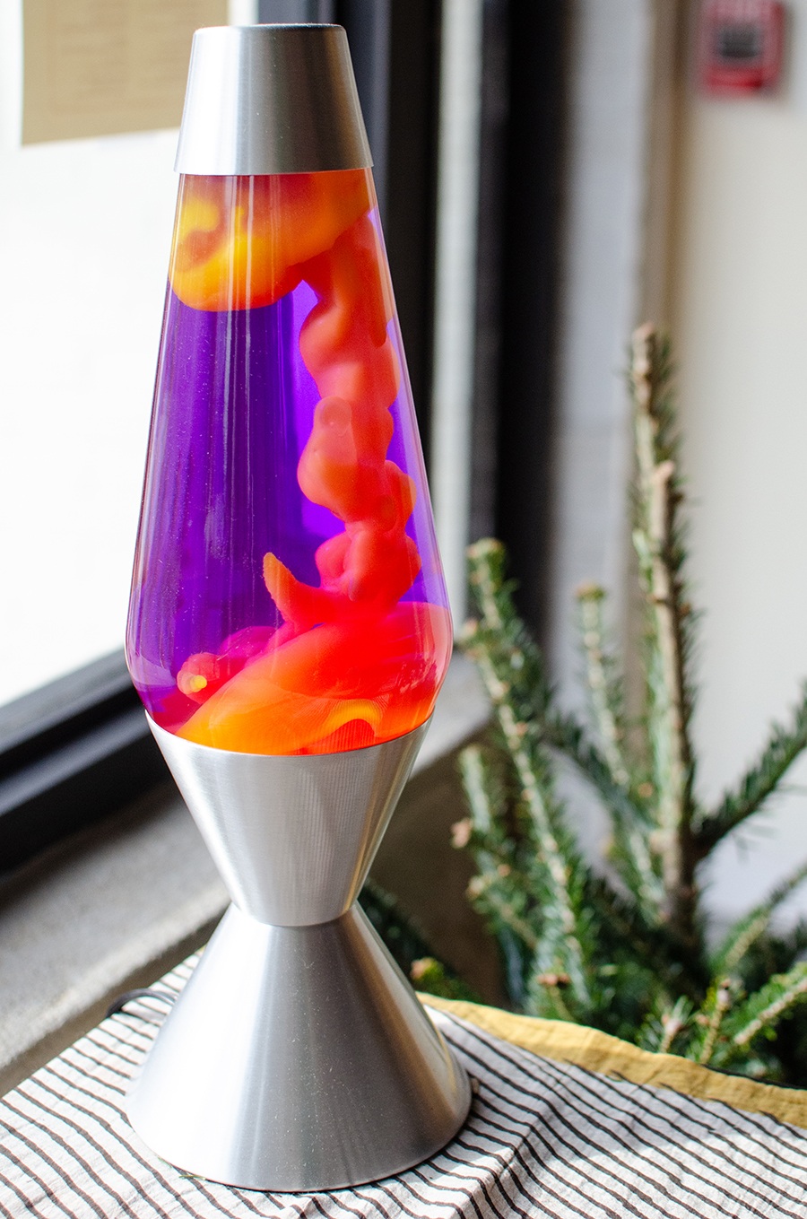 A pink and purple lava lamp sits on a counter atop a striped cloth.