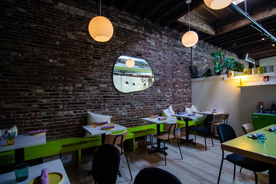 A restaurant dining room features a brick wall and green tables and benches.