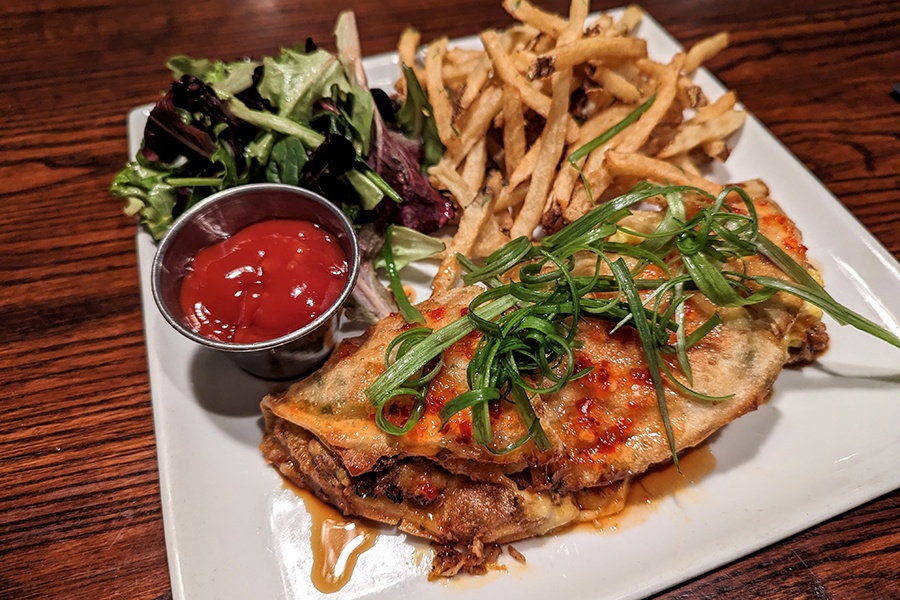 Pulled pork is stuffed inside a giant scallion pancake with sides of fries and mixed greens.