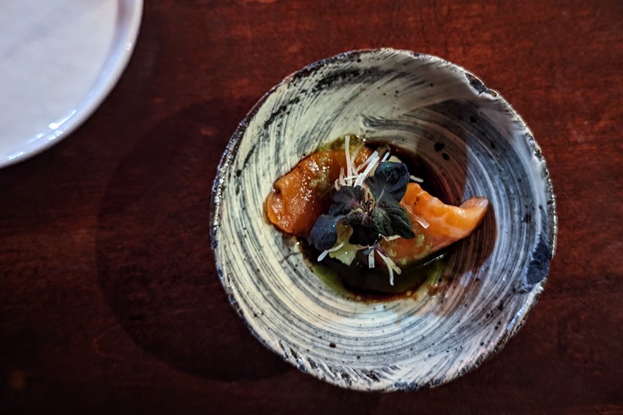 Overhead view of a slice of sashimi in a black and white bowl.