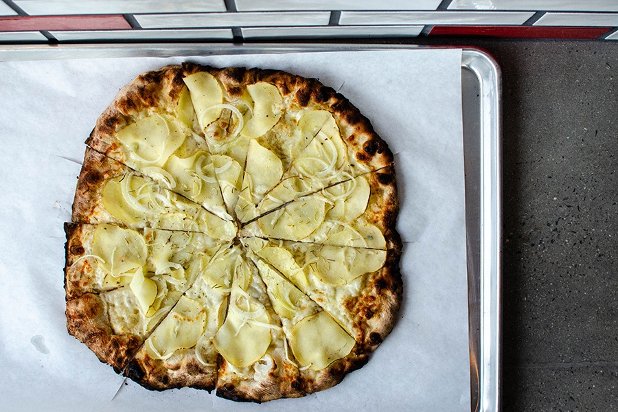 Overhead view of a white pizza with thin slices of potato and onions.